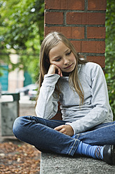 Germany, Berlin, Girl sitting in front of red brick wall - WESTF017473