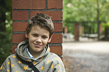 Germany, Berlin, Boy sitting in front of red brick wall - WESTF017482