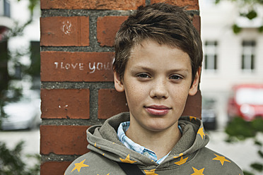 Germany, Berlin, Boy sitting in front of red brick wall - WESTF017484