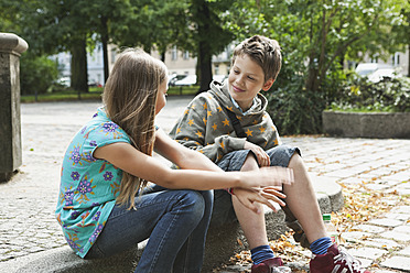 Germany, Berlin, Boy and girl sitting on curbstone - WESTF017491