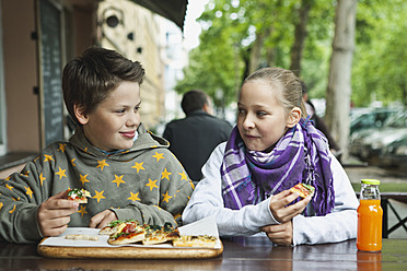 Germany, Berlin, Boy and girl eating pizza at cafe - WESTF017508