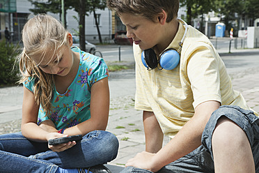 Germany, Berlin, Boy and girl sitting with cell phone and headphone - WESTF017513