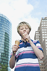 Germany, Berlin, Teenage boy eating ice cream in city - WESTF017517