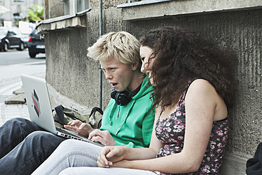 Deutschland, Berlin, Jugendliches Paar sitzt mit Laptop auf dem Gehweg - WESTF017521