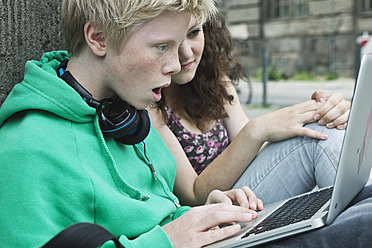 Deutschland, Berlin, Jugendliches Paar sitzt mit Laptop auf dem Gehweg - WESTF017522