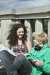 Deutschland, Berlin, Jugendliches Paar sitzt auf Brücke und liest - WESTF017529