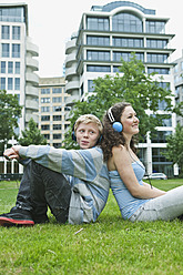 Germany, Berlin, Teenage couple with headphones listening music in park - WESTF017539