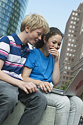 Germany, Berlin, Teenage couple using laptop in city - WESTF017546