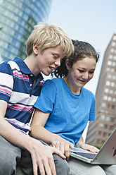 Germany, Berlin, Teenage couple using laptop in city - WESTF017547