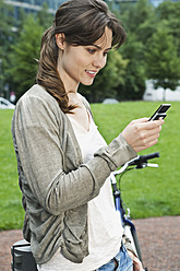 Deutschland, Berlin, Frau benutzt Mobiltelefon neben Fahrrad - WESTF017557