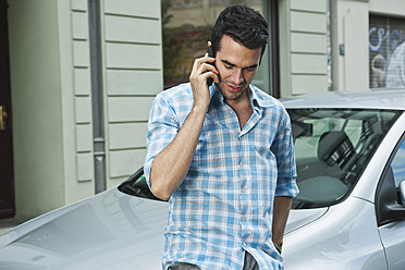 Deutschland, Berlin, Mann benutzt Mobiltelefon vor einem Auto - WESTF017563