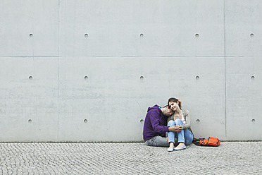 Deutschland, Berlin, Paar sitzt vor großer Mauer auf dem Gehweg - WESTF017587