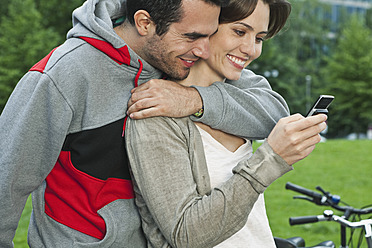 Germany, Berlin, Couple using cell phone in park - WESTF017591