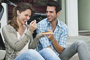 Germany, Berlin, Couple eating snacks on sidewalk - WESTF017609