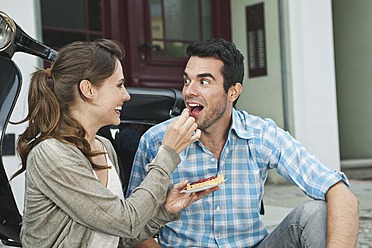 Germany, Berlin, Couple eating snacks on sidewalk - WESTF017611