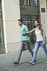 Germany, Berlin, Couple walking hand in hand through city street - WESTF017613