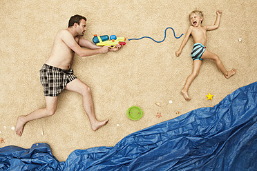 Deutschland, Vater und Sohn spielen mit Wasserpistolen am Strand - BAEF000291