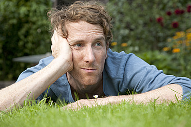 Man thinking while lying on grass in front of daisy - DBF000169