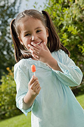 Germany, Bavaria, Huglfing, Girl holding lollipop in garden, smiling, portrait - RIMF000004