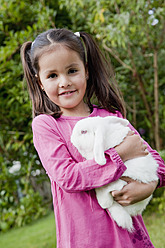 Deutschland, Bayern, Huglfing, Mädchen hält Kaninchen im Garten, lächelnd, Porträt - RIMF000007