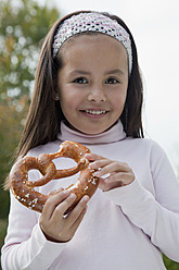 Germany, Bavaria, Huglfing, Girl holding pretzel in garden, smiling, portrait - RIMF000036