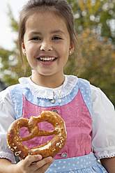 Deutschland, Bayern, Huglfing, Mädchen hält Brezel im Garten, lächelnd, Porträt - RIMF000040