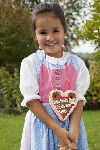 Deutschland, Bayern, Huglfing, Mädchen mit Lebkuchenherz im Garten, lächelnd, Porträt, lizenzfreies Stockfoto