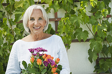 Germany, Bavaria, Senior woman holding flowers, smiling, portrait - WESTF017632