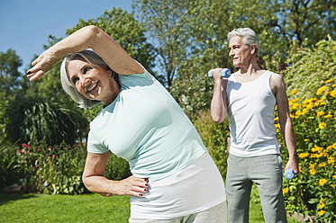 Germany, Bavaria, Mature man lifting dumbells, senior woman exercising, smiling - WESTF017642