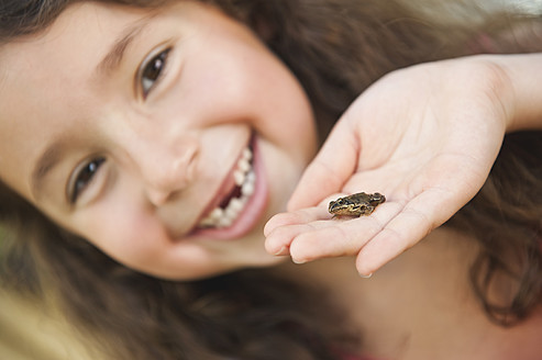 Germany, Bavaria, Human hand with little frog, girl smiling in background - WESTF017714