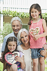 Germany, Bavaria, Grandparents with granddaughter holding gingerbread, smiling, portrait - WESTF017748