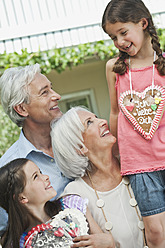 Germany, Bavaria, Grandparents with granddaughter holding gingerbread, smiling - WESTF017749