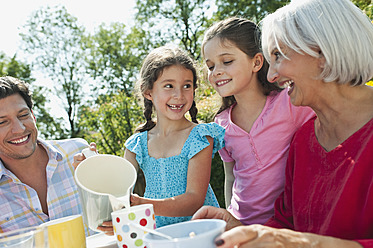 Germany, Bavaria, Family having coffee and cake in garden, smiling - WESTF017788