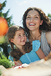 Germany, Bavaria, Mother and daughter at coffee table in garden, smiling - WESTF017800