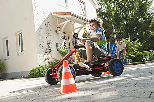 Deutschland, Bayern, Junge fährt Pedal-Gokart mit Eltern im Hintergrund - WESTF017810
