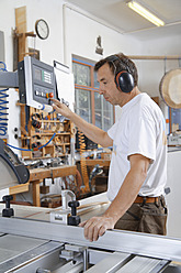Germany, Upper Bavaria, Schaeftlarn, Carpenter working on sawing machine - TCF001906