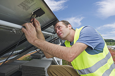 Deutschland, München, Techniker, der das Kabel eines Solarmoduls befestigt - WESTF017840