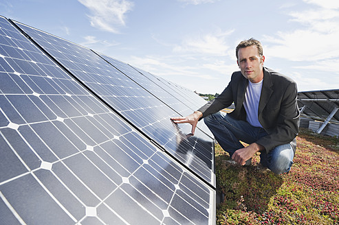 Deutschland, München, Mann berührt Solarpanel in Solaranlage, lächelnd, Porträt - WESTF017850