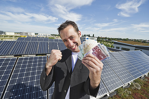 Deutschland, München, Mann mit Euro-Scheinen in Solaranlage, lächelnd, Porträt - WESTF017853