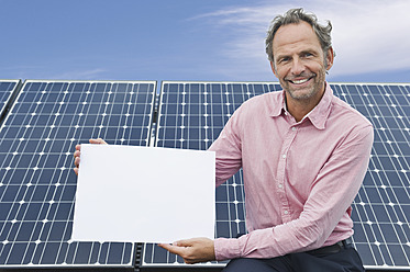 Deutschland, München, Älterer Mann hält leere weiße Tafel in Solaranlage, lächelnd, Porträt - WESTF017854