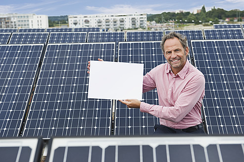 Deutschland, München, Älterer Mann hält leere weiße Tafel in Solaranlage, lächelnd, Porträt - WESTF017855