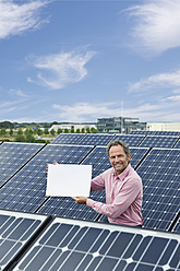 Deutschland, München, Älterer Mann hält leere weiße Tafel in Solaranlage, lächelnd, Porträt - WESTF017856