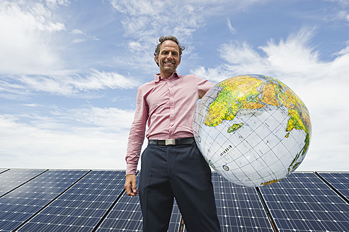 Deutschland, München, Älterer Mann hält Globus in Solaranlage, lächelnd, Porträt - WESTF017866