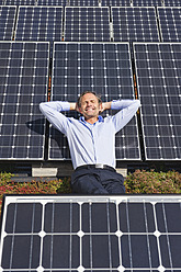 Deutschland, München, Älterer Mann, der lächelnd auf einem Panel in einer Solaranlage ruht - WESTF017871