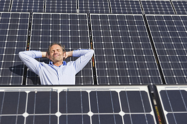 Deutschland, München, Älterer Mann, der lächelnd auf einem Panel in einer Solaranlage ruht - WESTF017872