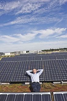 Deutschland, München, Älterer Mann, der lächelnd auf einem Panel in einer Solaranlage ruht - WESTF017873