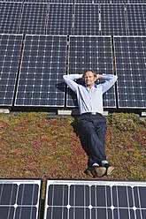 Germany, Munich, Mature man resting on panel in solar plant, smiling - WESTF017874