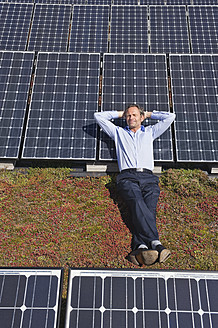 Deutschland, München, Älterer Mann, der lächelnd auf einem Panel in einer Solaranlage ruht - WESTF017874