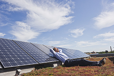 Germany, Munich, Mature man resting on panel in solar plant, smiling - WESTF017875