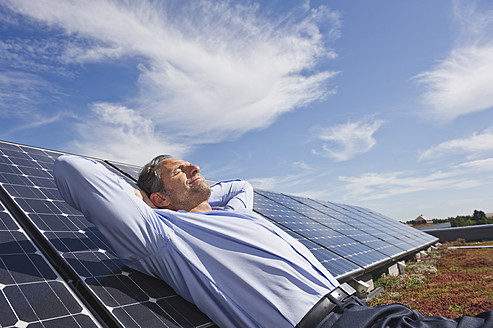 Deutschland, München, Älterer Mann, der lächelnd auf einem Panel in einer Solaranlage ruht - WESTF017876